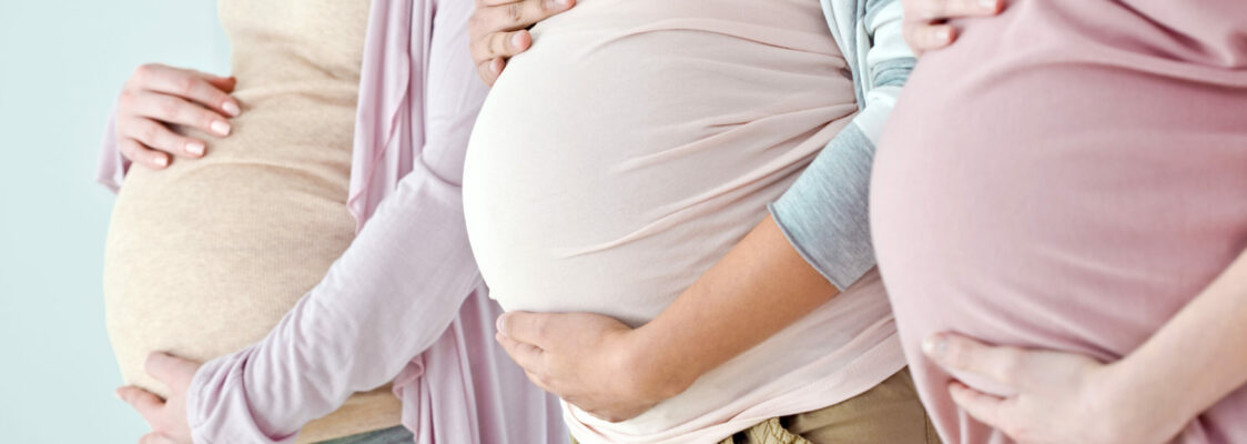 Close-up of the pregnant bellies of a three women standing in a row. Selective focus.
