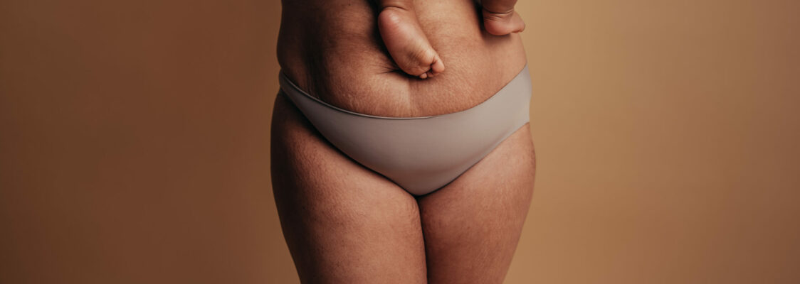 Cropped shot of a healthy female carrying her baby. Close-up of a woman in underwear with feet of child on postpartum belly.