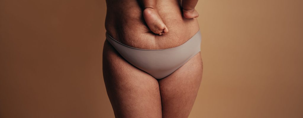 Cropped shot of a healthy female carrying her baby. Close-up of a woman in underwear with feet of child on postpartum belly.